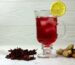 Zobo drink in a glass cup with lemon slice on the glass and zobo leaves, ginger and cinnamon on the table